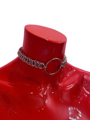 A close-up of a simple silver chain choker with a bold ring at the center. The sleek, minimalist design rests elegantly against a neutral backdrop, highlighting its refined and timeless appeal.